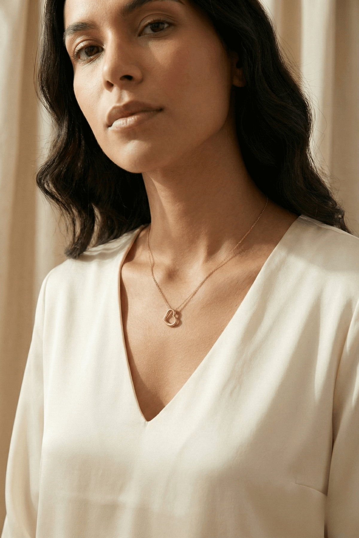 Kadın model, 14 ayar altın kalpli kolye takarken, şık bir bluz giymiş.